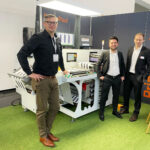 Paul Arndt, PrintsPaul; Christian Kröger, BST und Christian Dotzler, Nyquist Systems, am PrintsPaul-Stand auf der ICE Europe. Im Hintergrund die Konfektioniermaschine PPVSA420 mit einem TubeScan 100%-Inspektionssystem mit 4k-Kamera (Quelle: PrintsPaul)